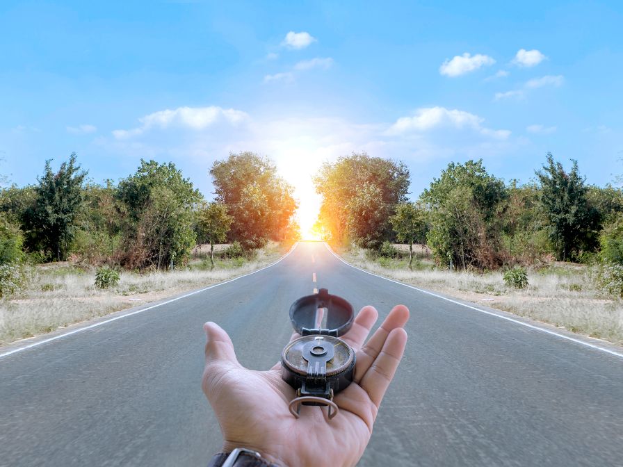 Hand holding compass on highway to sunset